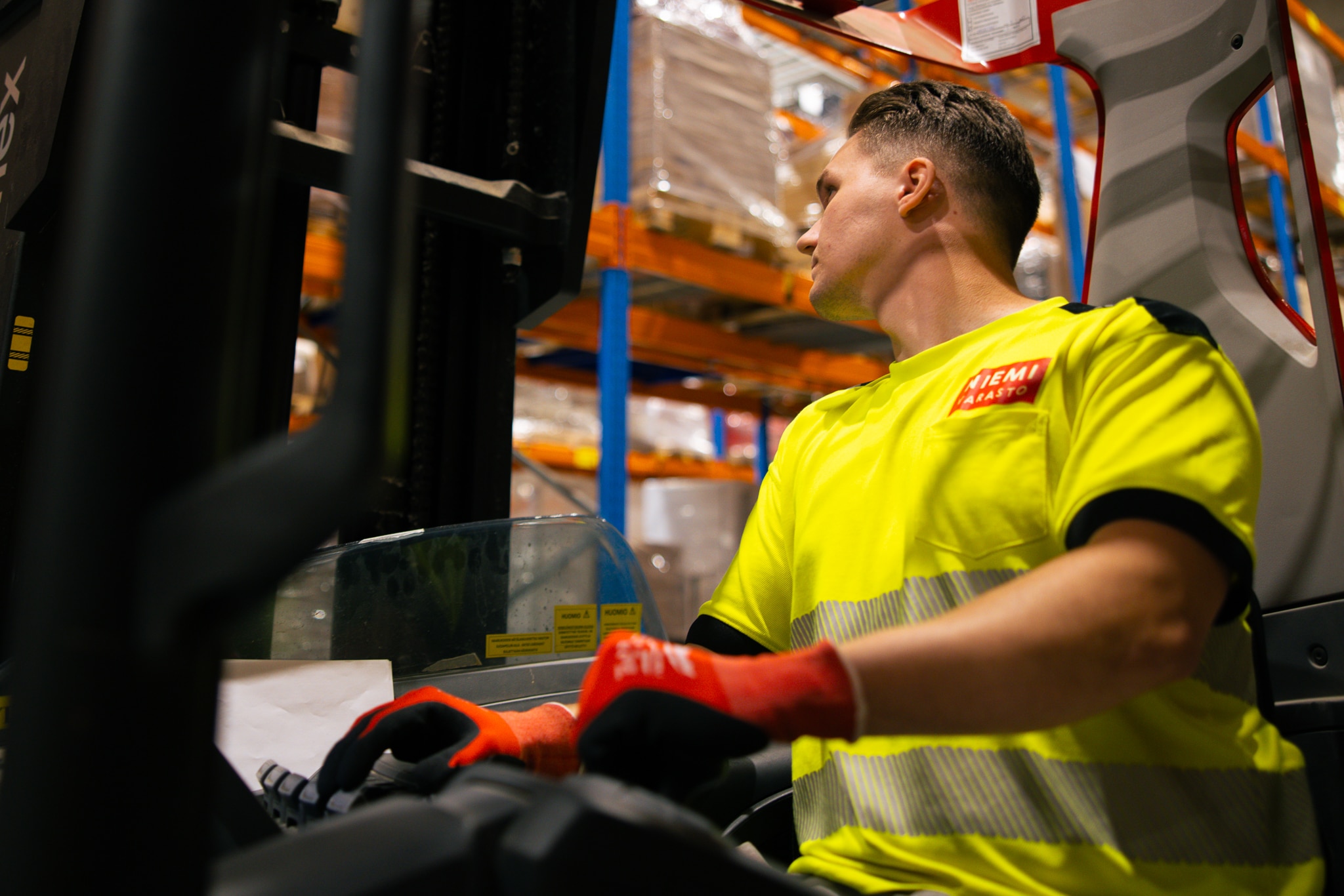 Varastohenkilö keltaisessa paidassa ajaa trukkia