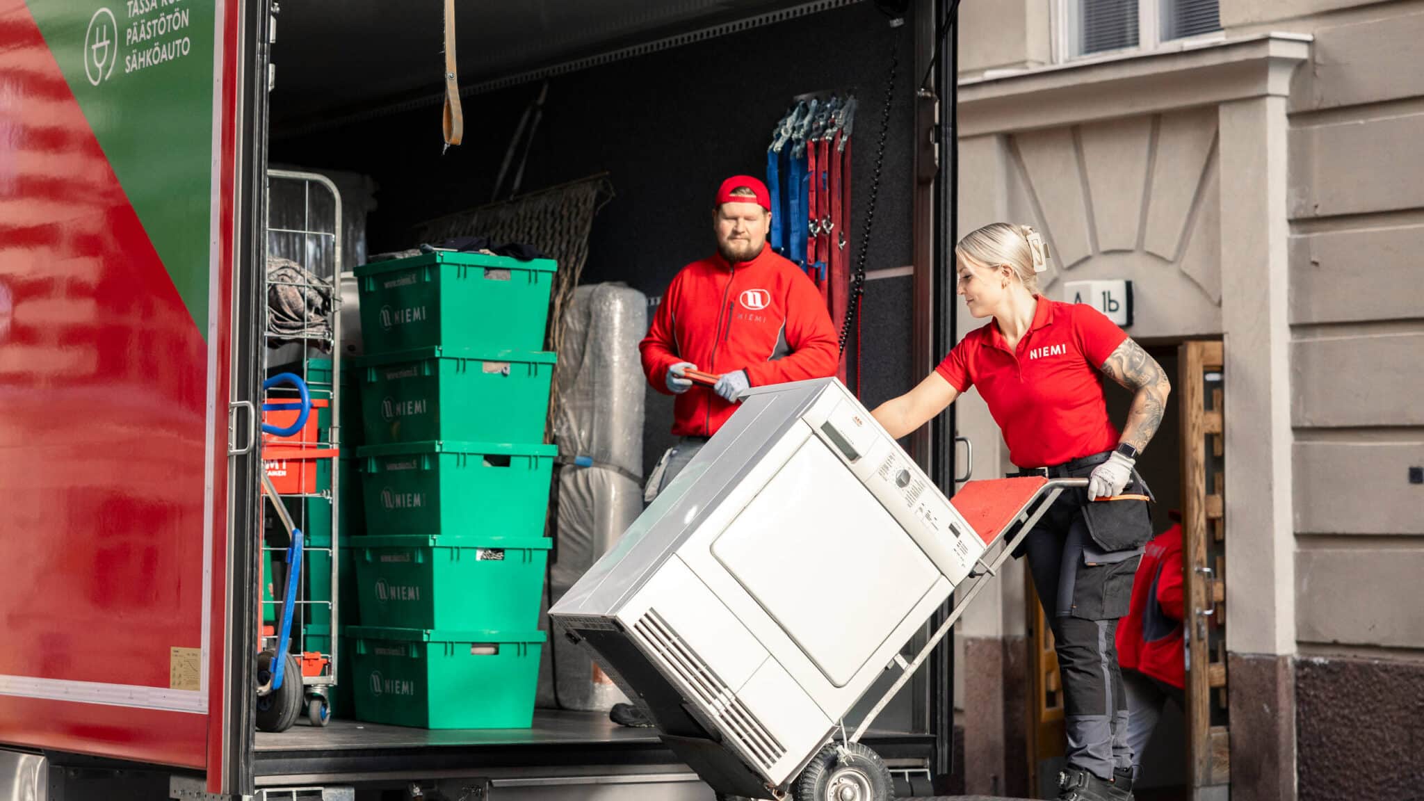 Pesukoneen, muuttaja ja kuljettaja muuttoauton perälaudalla